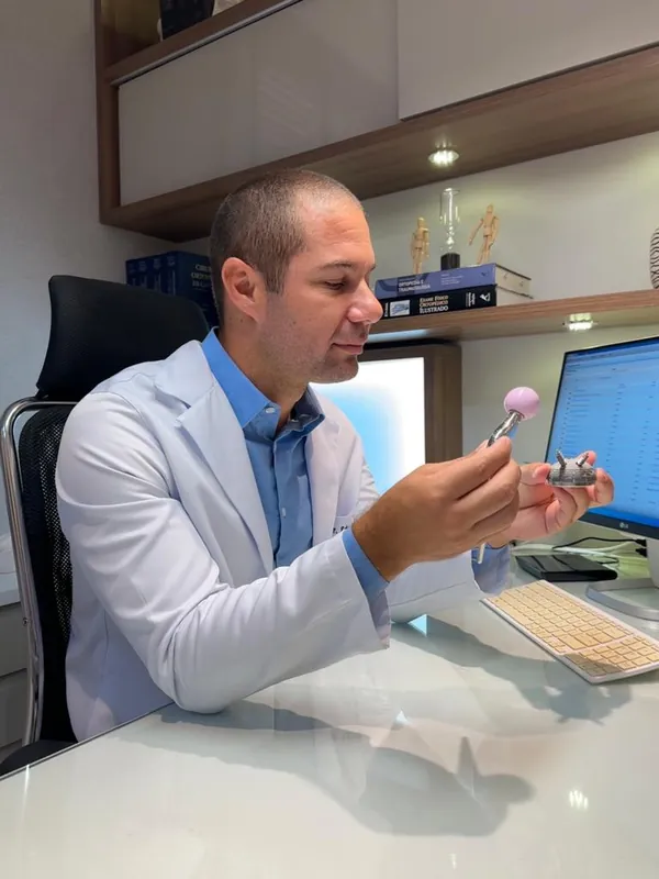 Dr. Eduardo Medeiros com um modelo de prótese do quadril no consultório